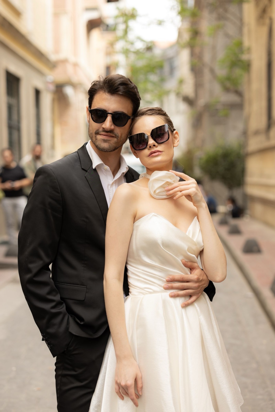 A couple in elegant wedding attire on a warm city street.