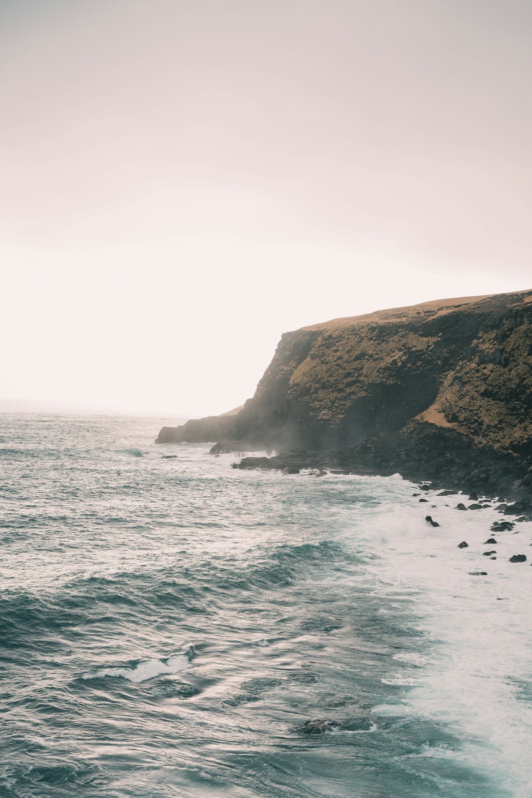 Waves breaking beneath a green coastal cliff.
