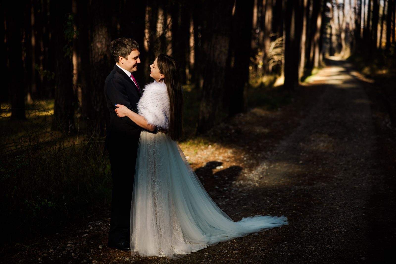 A wedding couple embracing in a sunlit forest.