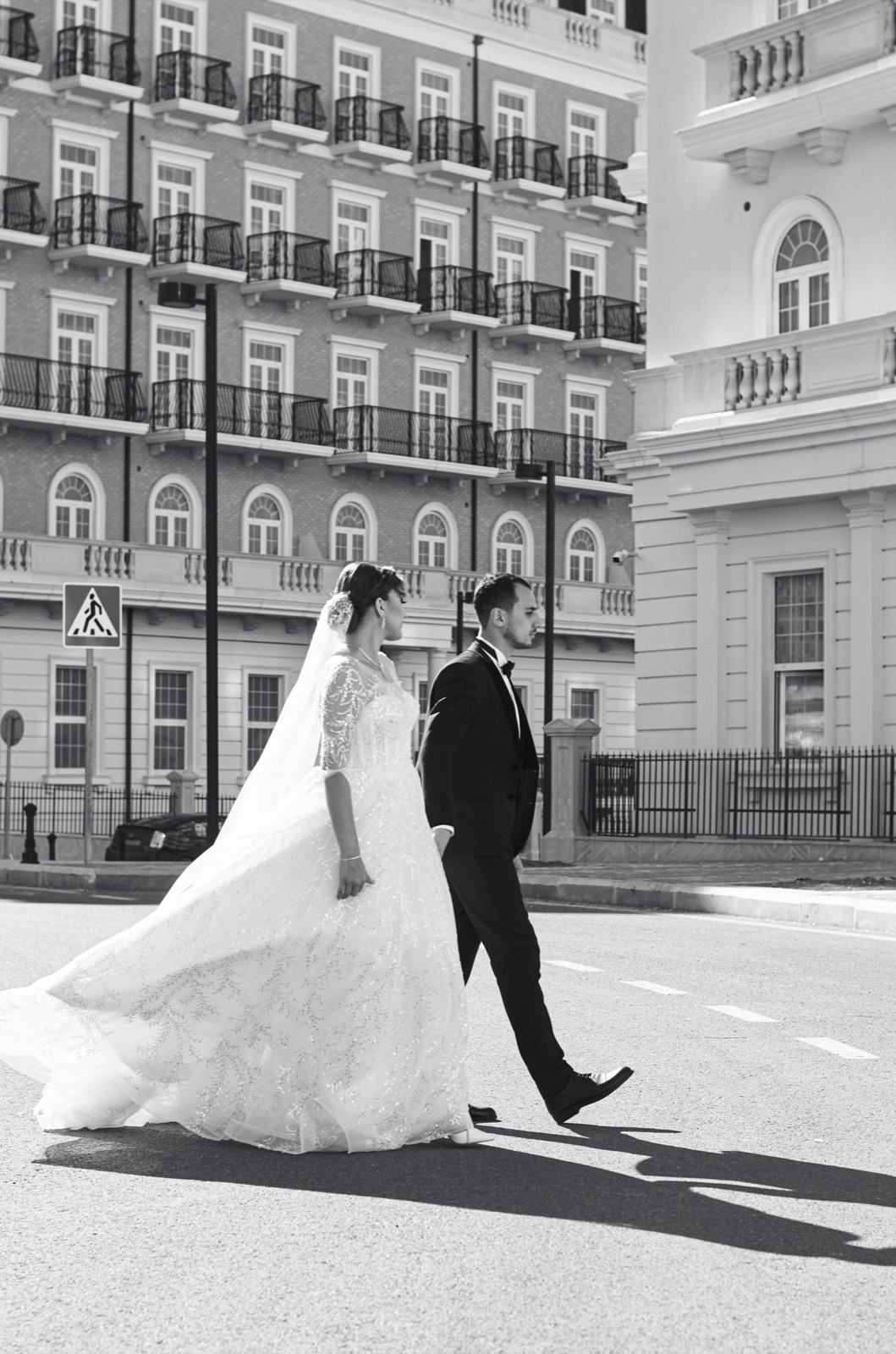 A bride and groom walking across a city square, photographed in black and white.