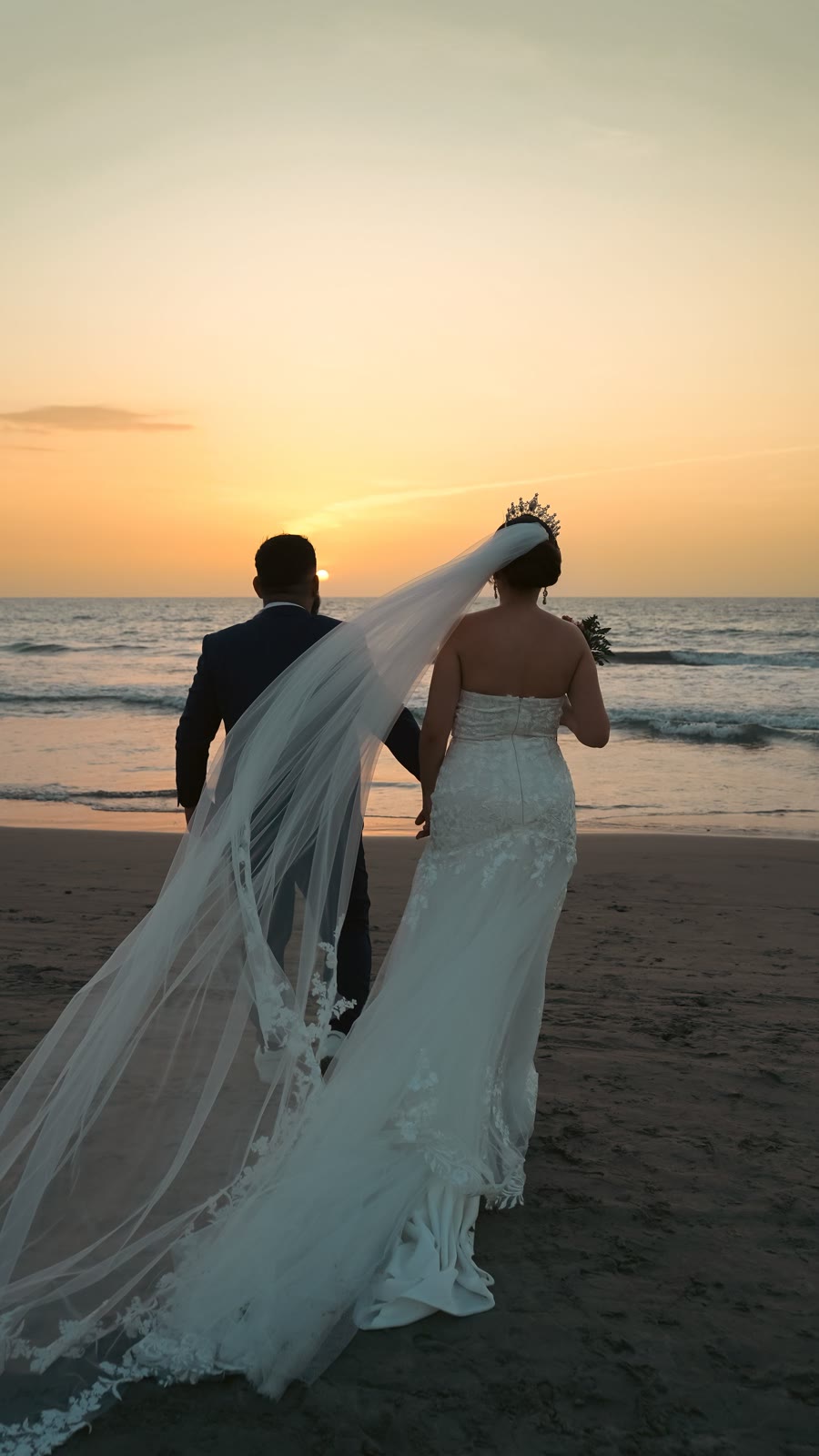 A wedding couple walking beside the sea at sunset